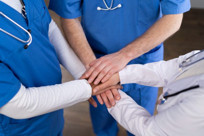 Multidisciplinair team in een revalidatietraject Zorgprofessionals uit een multidisciplinair team houden de handen op elkaar als symbool hiervan.